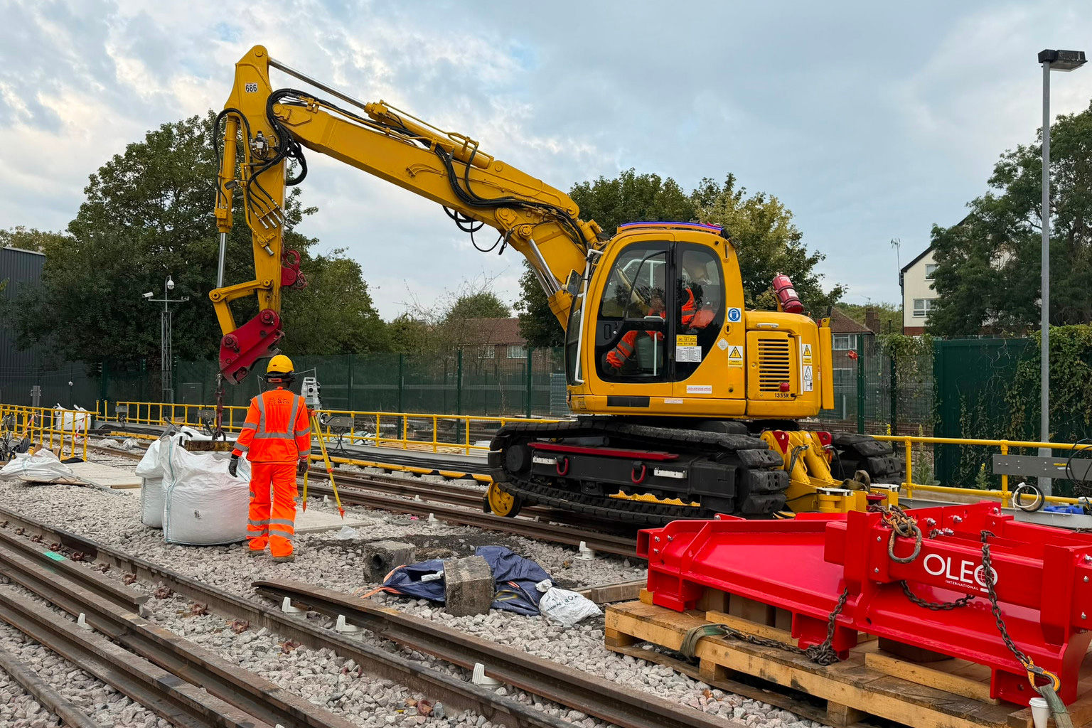 AJ rail worker beside a road-rail excavator during trackside lifting work
