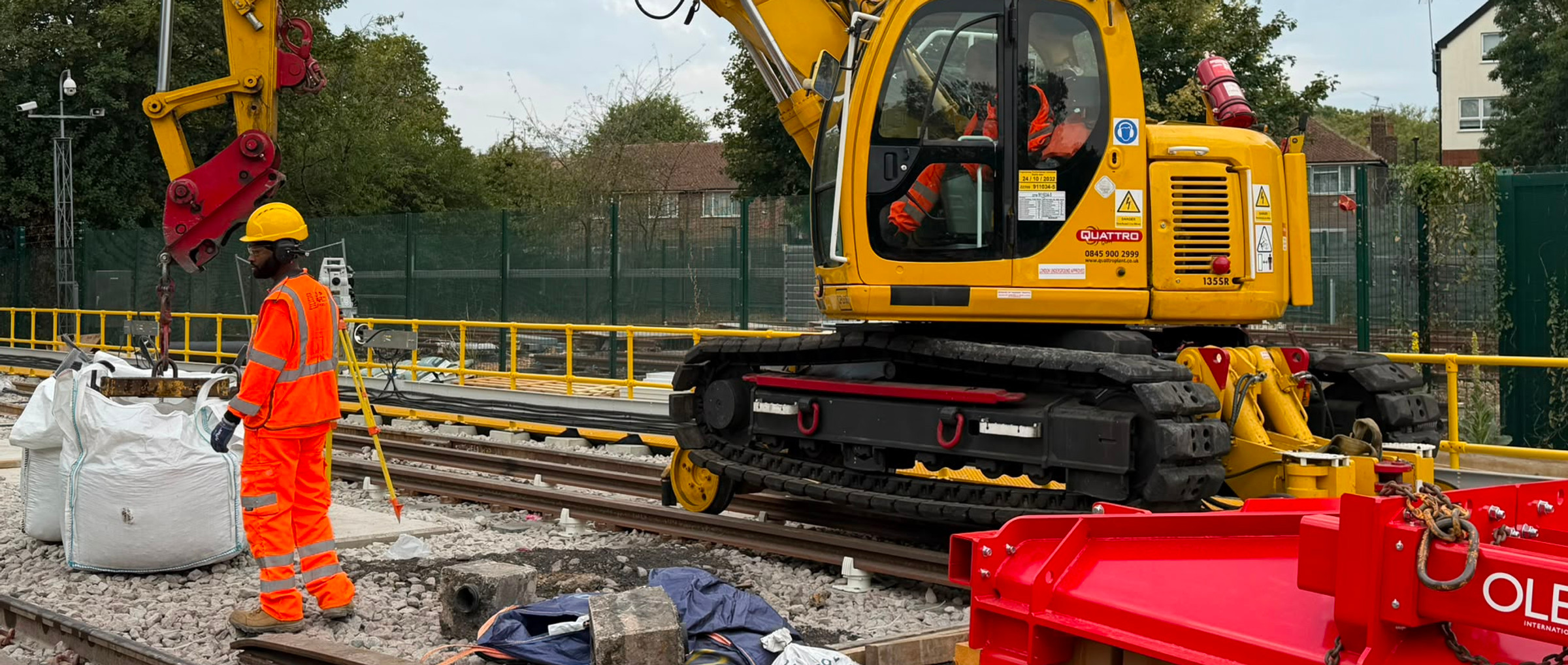 Rail worker beside a yellow road-rail excavator and lifting attachment