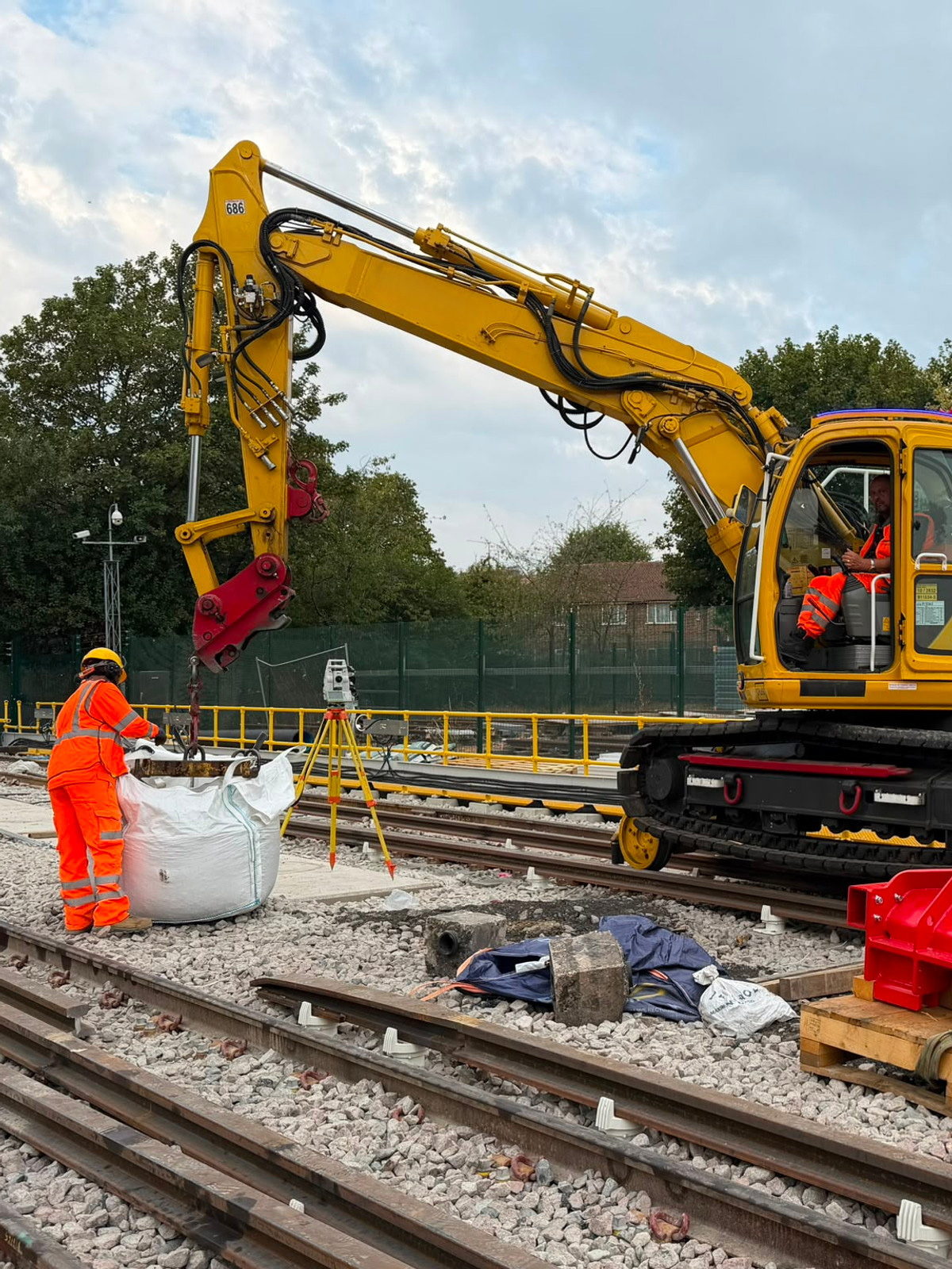 Excavator operator and trackside worker handling a bulk bag beside the railway