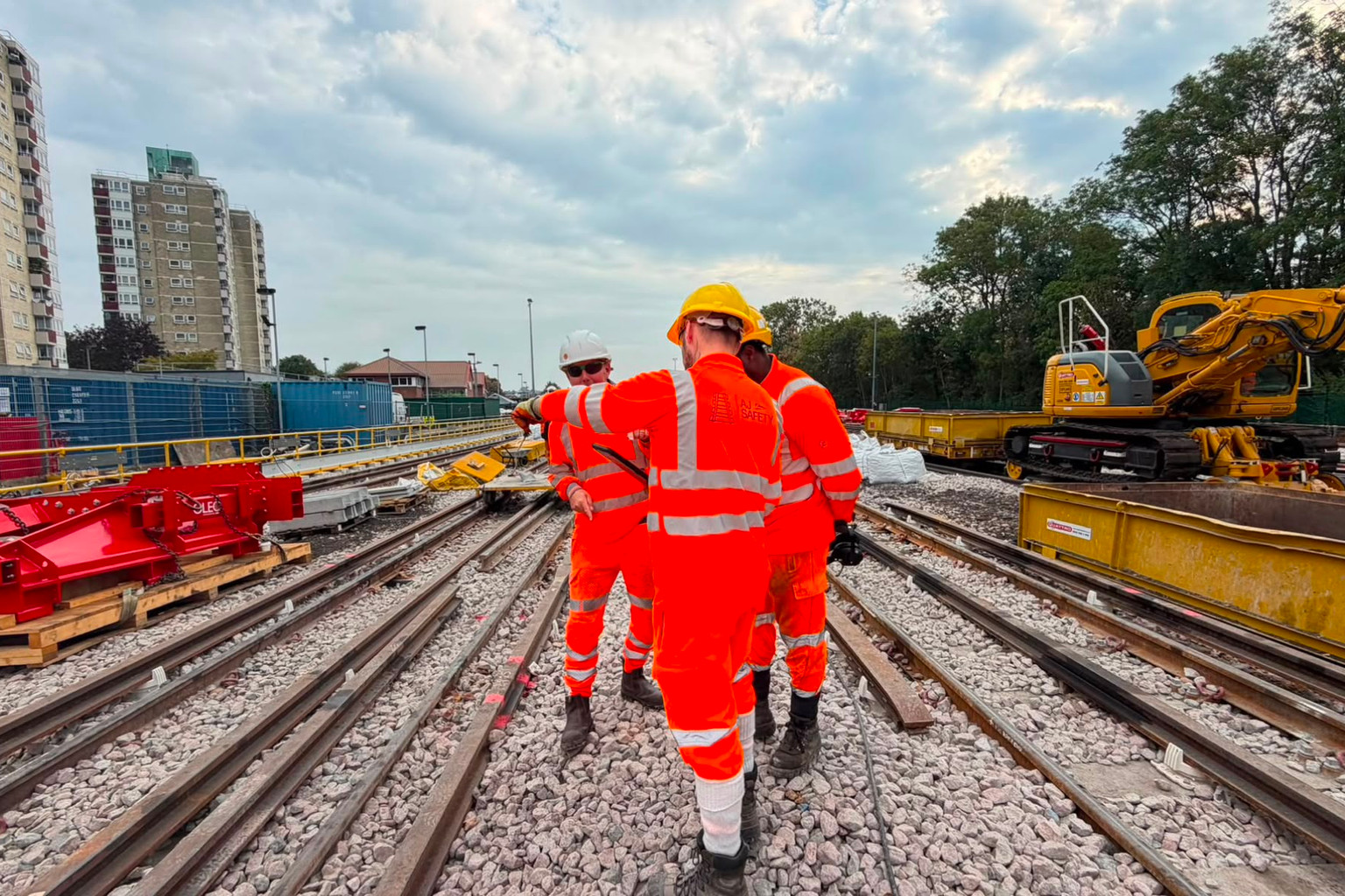 AJ personnel beside a rail worksite with track equipment in the background