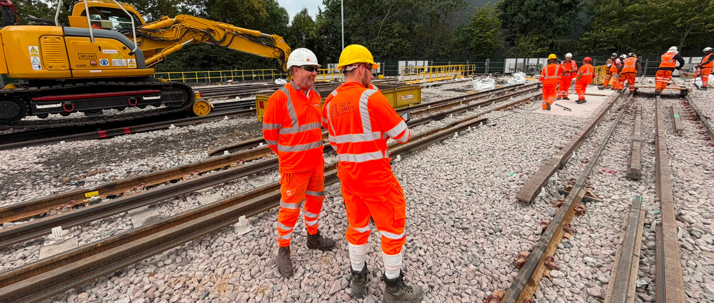 AJ Safety Services personnel in orange workwear beside tracks and rail plant