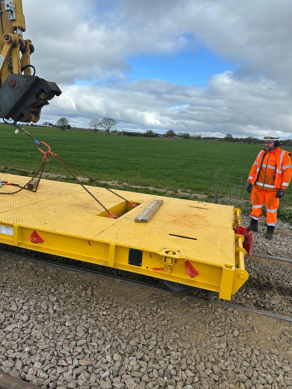 Rail safety worker monitoring an excavator lift in a controlled infrastructure worksite