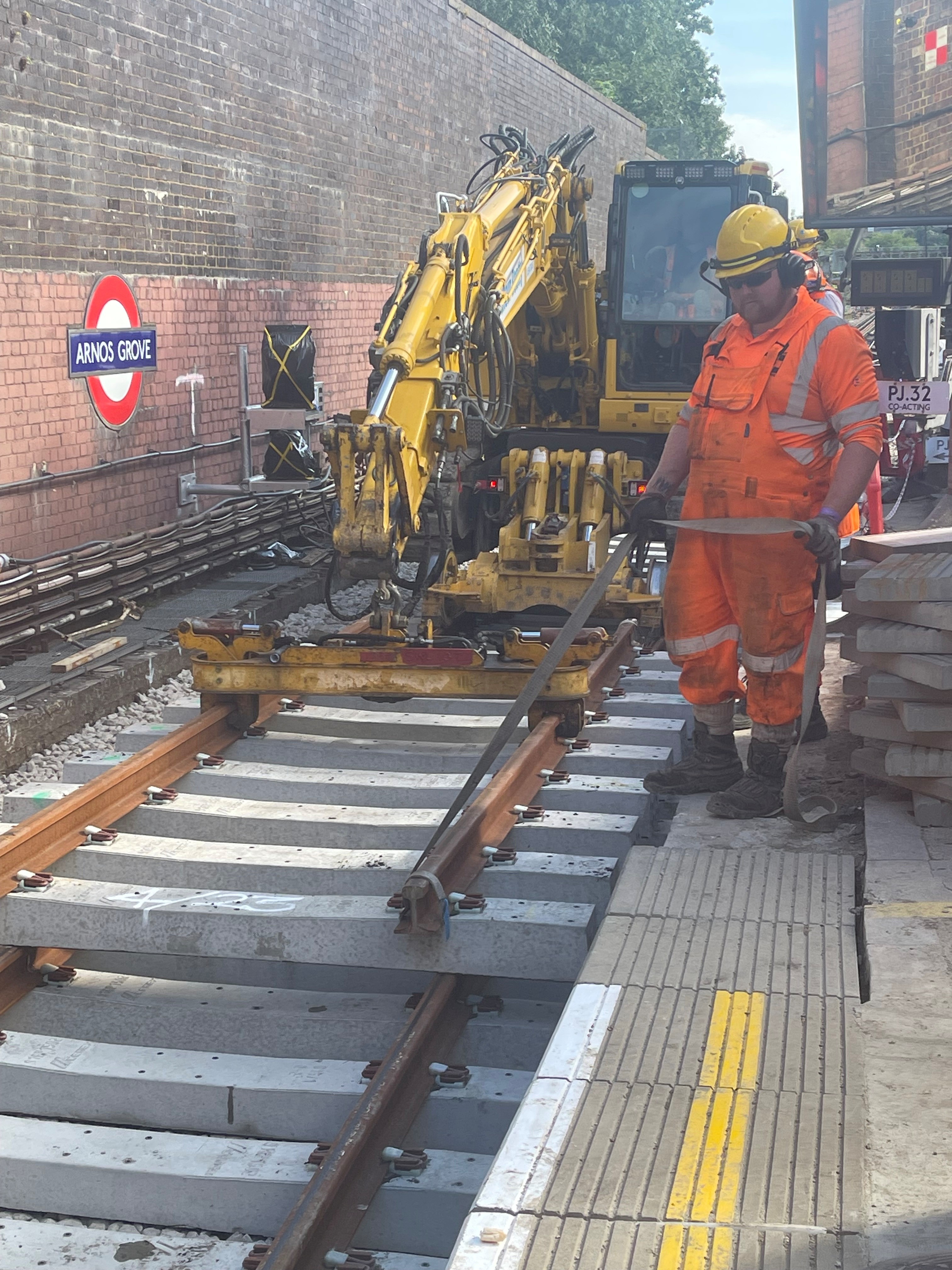 Rail worker coordinating a road-rail excavator beside a London Underground platform