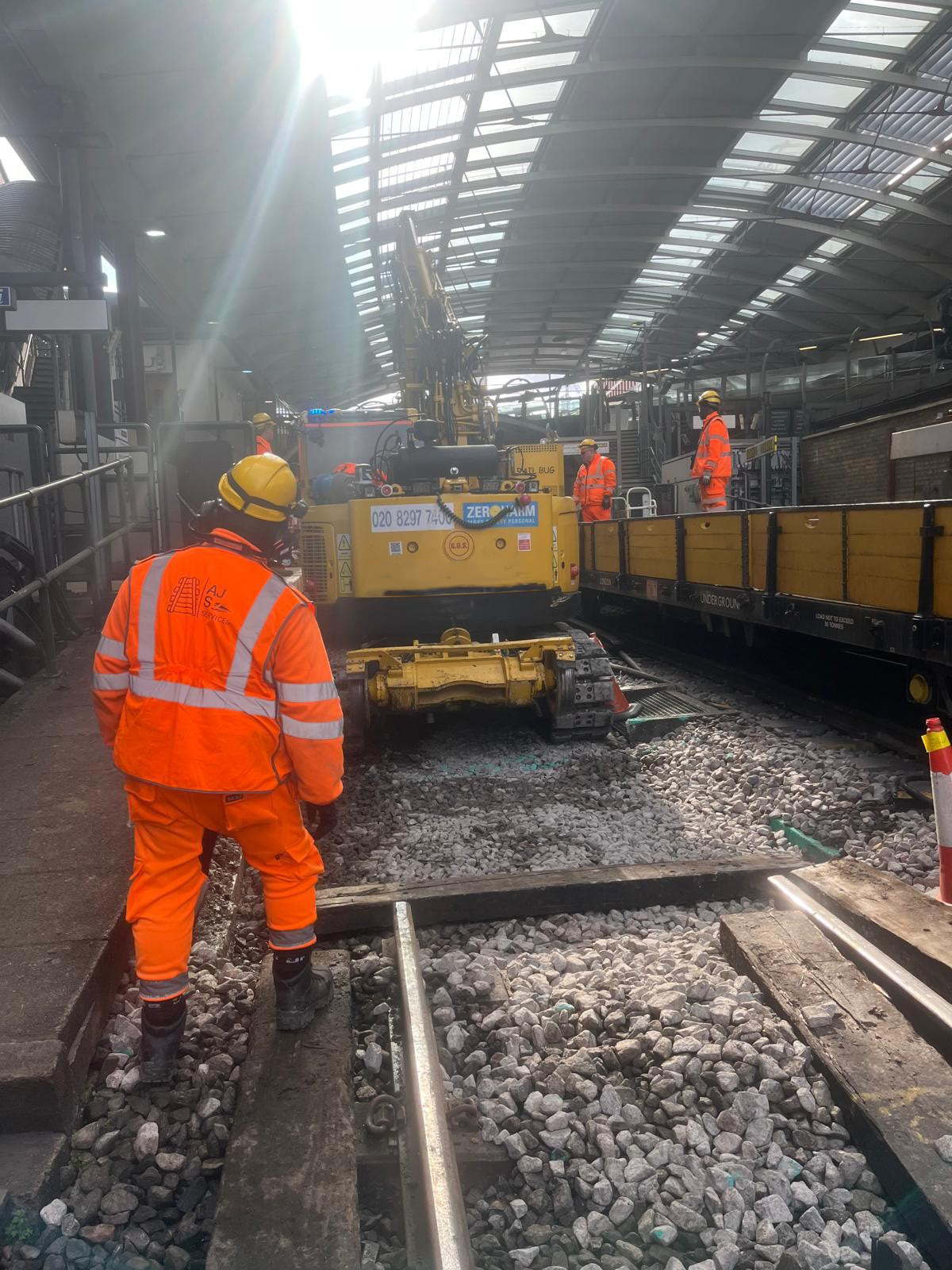Rail worker overseeing ballast and plant activity inside a London Underground station